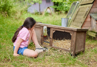 Une fille est assise sur l’herbe près d’un clapier en bois à la ferme BoerenBed New Barn Farm, Est d’Angleterre.