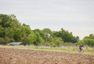 En person cykler langs en mark i BoerenBed New Barn Farm, omgivet af grønne træer og et skur i England.