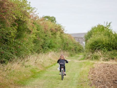 Un niño monta en bicicleta por un sendero verde rodeado de arbustos en BoerenBed New Barn Farm, Inglaterra.