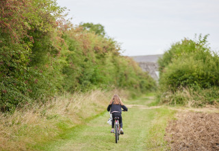 Et barn cykler på en grøn sti omgivet af buske ved BoerenBed New Barn Farm feriepark i Østengland.