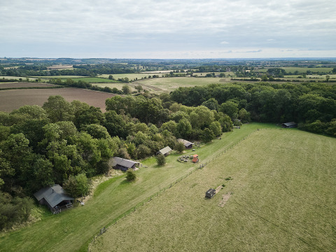 Luftfoto af BoerenBed New Barn Farm feriepark i det østlige England med telte ved skovkanten