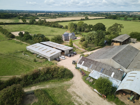 Vista aérea del parque de vacaciones BoerenBed New Barn Farm en el este de Inglaterra, con graneros y campos verdes.