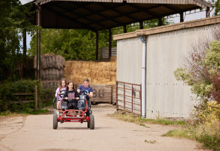 Tre børn cykler på en firehjulet gokart ved et landbrug med halmballer på BoerenBed New Barn Farm.