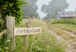 Letrero de madera que dice 'Featherdown' en un camino rural en BoerenBed Manor Farm, al sureste de Inglaterra.