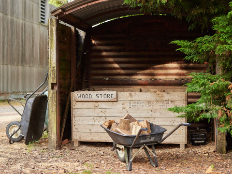Cobertizo para leña y carretilla con madera en BoerenBed Manor Farm, en el sureste de Inglaterra.