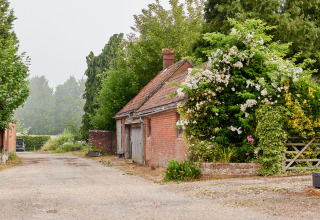 A quaint country farm with an old barn, lush trees, and blooming bushes in South East England, UK.