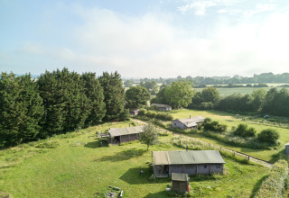 View of BoerenBed Manor Farm holiday park in South East England with fields, trees and rural cabins.