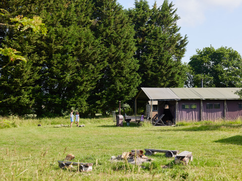 Twee mensen bij een tent op BoerenBed Manor Farm vakantiepark in Zuidoost-Engeland, omringd door bomen.