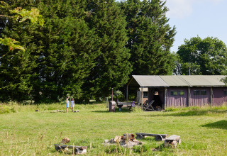 Dos personas cerca de una tienda en BoerenBed Manor Farm en el sureste de Inglaterra, rodeados de árboles.