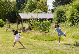 Zwei Mädchen spielen Schlagball auf einer Wiese vor einem Zelt im BoerenBed Manor Farm Ferienpark, Südostengland.