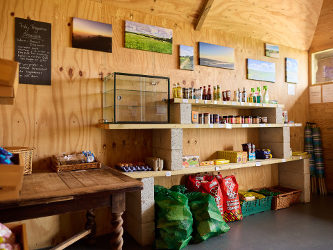 Farm shop at Treganhoe Farm, South West England, with wooden shelves, groceries, and scenic wall photos.