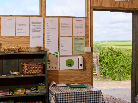 Vista interior con tablón de anuncios y mesa en BoerenBed Treganhoe Farm, con campo visible al fondo.