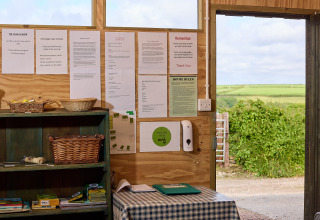 Innenaufnahme eines Infoboards und Tisches bei BoerenBed Treganhoe Farm mit Blick ins grüne Umland.