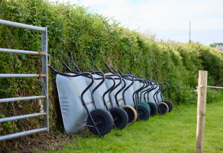 Mehrere Schubkarren lehnen an einer Hecke bei BoerenBed Treganhoe Farm in Südwestengland im Freien.