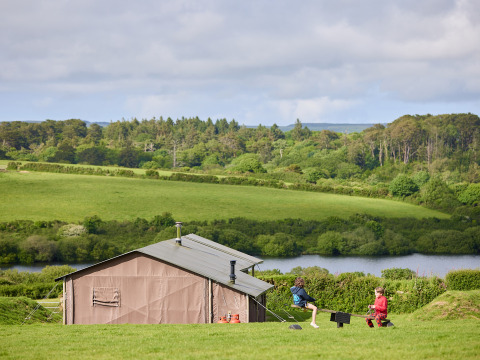 Children playing outside a glamping tent at BoerenBed Treganhoe Farm, set in lush green hills and countryside.