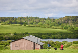 Bambini giocano fuori da una tenda glamping a BoerenBed Treganhoe Farm, tra colline e boschi verdi.