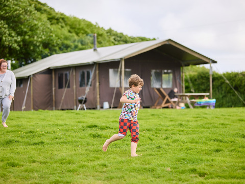 Child running barefoot on the grass at BoerenBed Treganhoe Farm holiday park in South West England, UK.