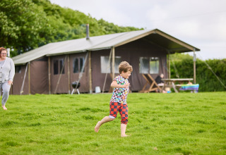 Kind rennt barfuß auf der Wiese vor einem Zelt bei BoerenBed Treganhoe Farm, einem Ferienpark in Südwestengland.