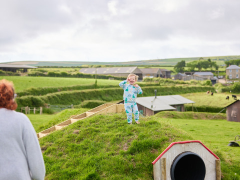 Ein kleines Kind im blauen Pyjama spielt auf einem Hügel auf dem Bauernhof BoerenBed Treganhoe, Südwestengland.