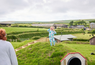 Un jeune enfant en pyjama bleu joue joyeusement sur une colline verdoyante à BoerenBed Treganhoe Farm, Angleterre.