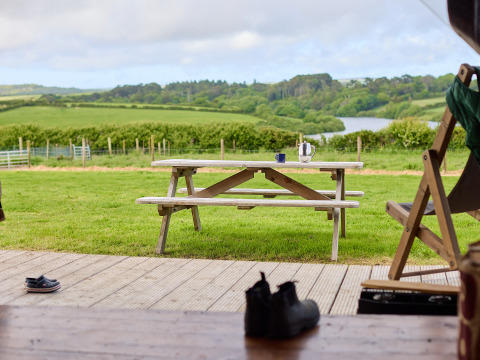 View from a deck with table and chairs onto a green field at BoerenBed Treganhoe Farm, South West England.