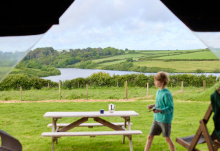 Blick auf grüne Felder und einen See im BoerenBed Treganhoe Farm Ferienpark, mit Kind und Picknicktisch.