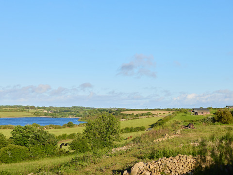 Scenic view of green fields, lake and buildings at BoerenBed Treganhoe Farm holiday park in South West England.