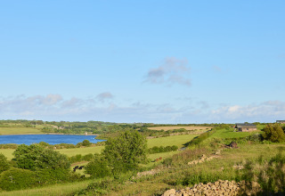Blick auf grüne Felder, See und Gebäude bei BoerenBed Treganhoe Farm Ferienpark in Südwestengland, Großbritannien.