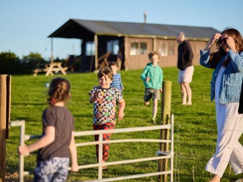 Des enfants courent et jouent sur l’herbe devant un lodge au BoerenBed Treganhoe Farm, sud-ouest de l’Angleterre.