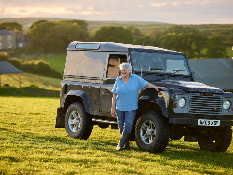 Une femme âgée se tient près d’un Land Rover sur l’herbe à la ferme Treganhoe dans le sud-ouest de l’Angleterre.