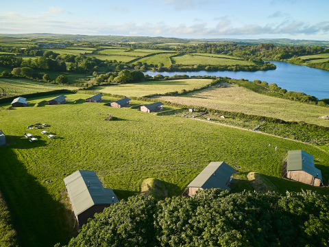 Luftfoto af BoerenBed Treganhoe Farm-feriepark i det sydvestlige England med grønne marker og sø.
