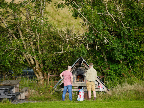 Deux hommes près d’un foyer extérieur à BoerenBed Pant y March Farm, un parc de vacances au Pays de Galles, Royaume-Uni.