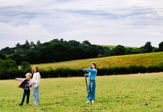 Children and an adult explore a grassy field at BoerenBed Lunsford Farm, a holiday park in South East England.