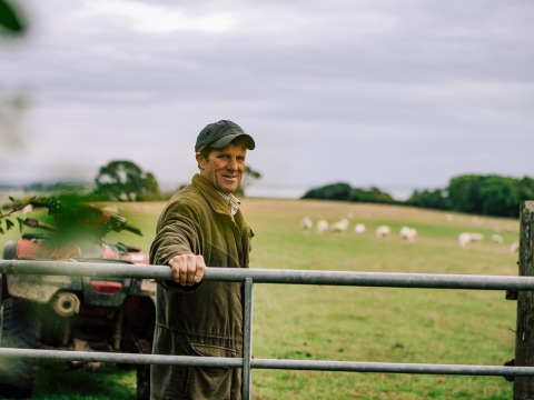 Un agriculteur debout près d’une barrière à BoerenBed Lunsford Farm, sud-est de l’Angleterre, moutons en fond.
