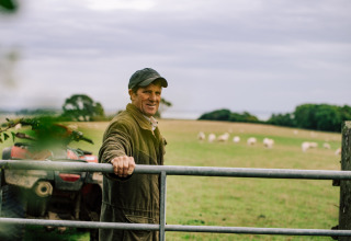 Een landbouwer bij een hek op BoerenBed Lunsford Farm in Zuidoost-Engeland, met schapen in de achtergrond.