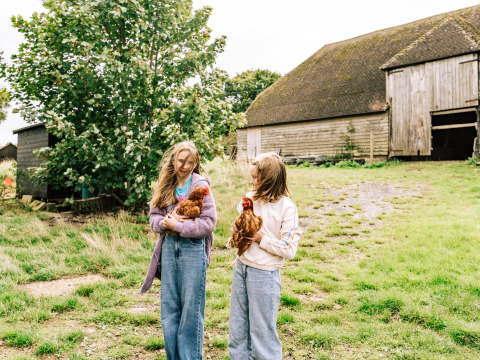 Dos niñas sostienen gallinas delante de un granero en BoerenBed Lunsford Farm, en el sureste de Inglaterra.