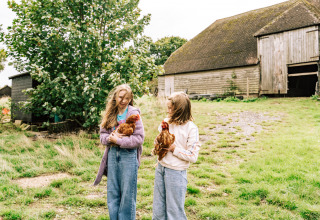 Zwei Mädchen halten Hühner vor einer Scheune im BoerenBed Lunsford Farm Ferienpark in Südostengland.
