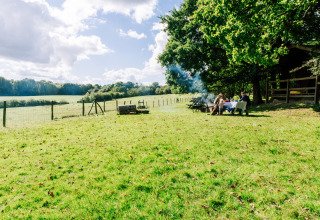 Zwei Personen genießen eine Mahlzeit an einem Tisch unter Bäumen auf einer sonnigen Wiese bei Sunninglye Farm.