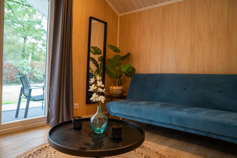 Cozy living area in Tiny House Deluxe with blue sofa, round table, and glass doors at Holiday park Latour.