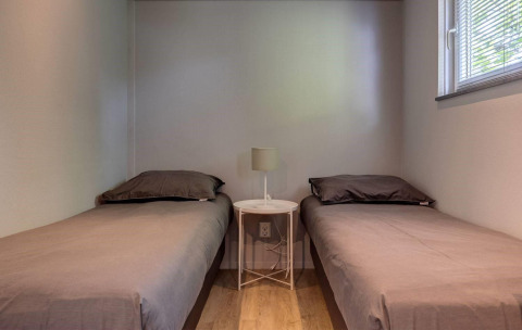 Two single beds, small round table with lamp, and a window in the Tiny House Deluxe at Latour park.