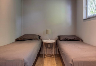 Two single beds, small round table with lamp, and a window in the Tiny House Deluxe at Latour park.