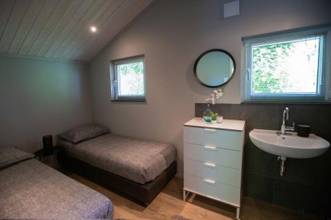 Dormitorio pequeño moderno con dos camas individuales, cómoda, lavabo y ventanas en Tiny House Deluxe, Países Bajos.