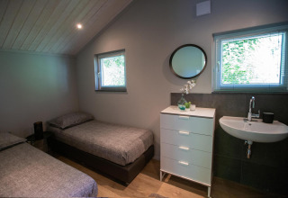 Moderna piccola camera da letto con due letti singoli, cassettiera, lavandino e finestre al Tiny House Deluxe nei Paesi Bassi.