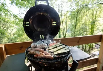 Grillmad tilberedes på en safari teltterrasse med udsigt over skoven, inklusive pølser og grøntsager.