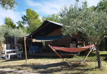 Tienda safari al aire libre con hamaca y mesa de picnic en Camping Pian di Boccio, Italia, rodeada de árboles.