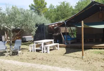 Vista exterior de una tienda safari con baño en Camping Pian di Boccio en Italia, rodeada de vegetación.