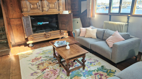 Salon sur la péniche De Zwerver à Marina Parcs Naarden, Pays-Bas, avec canapé, TV et vue sur l'eau.