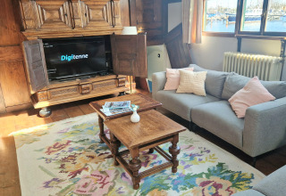 Salon sur la péniche De Zwerver à Marina Parcs Naarden, Pays-Bas, avec canapé, TV et vue sur l'eau.
