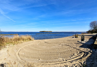 Foto vom Sandstrand an einem See mit klar blauem Himmel und Bäumen, aufgenommen bei einer Glamping-Unterkunft.