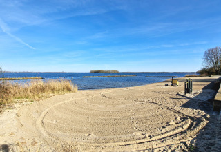 Foto vom Sandstrand an einem See mit klar blauem Himmel und Bäumen, aufgenommen bei einer Glamping-Unterkunft.